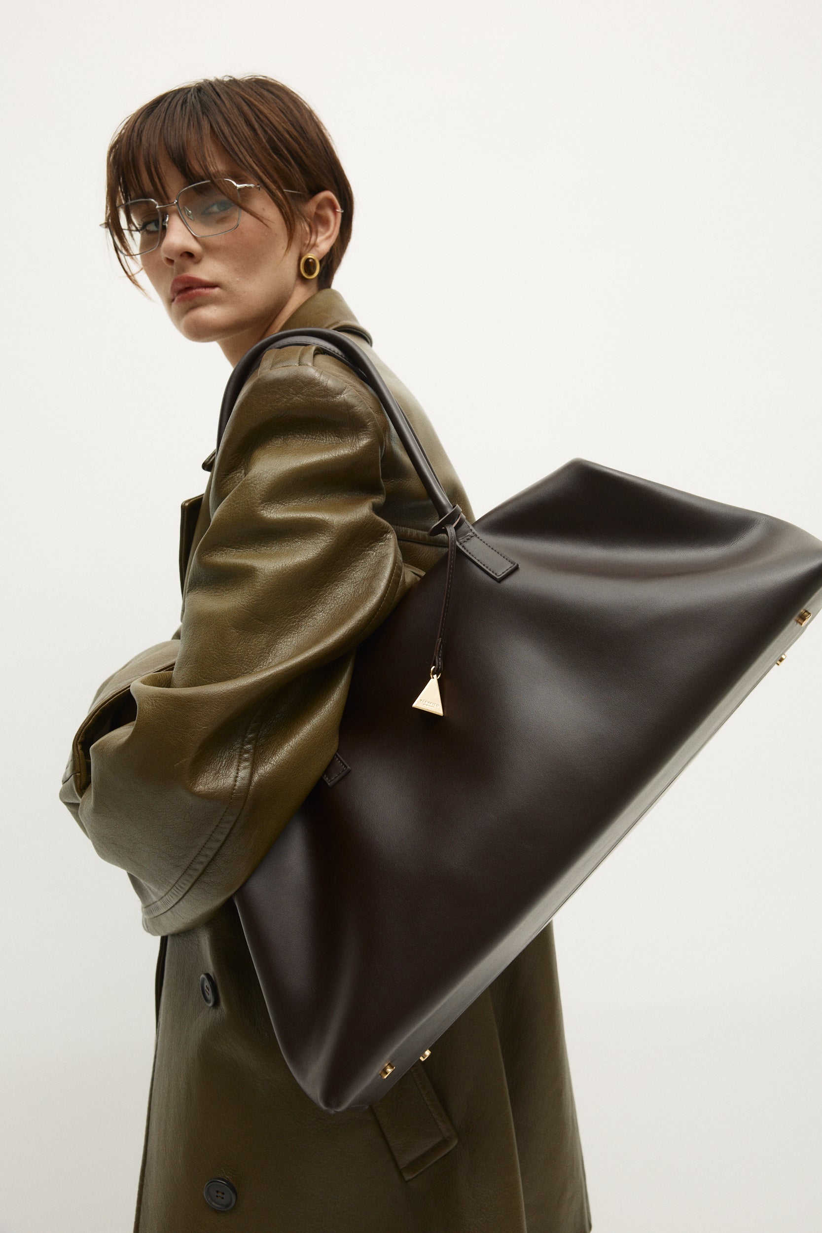Person wearing a green coat holding a large Chocolate Club Large Handbag against a white background