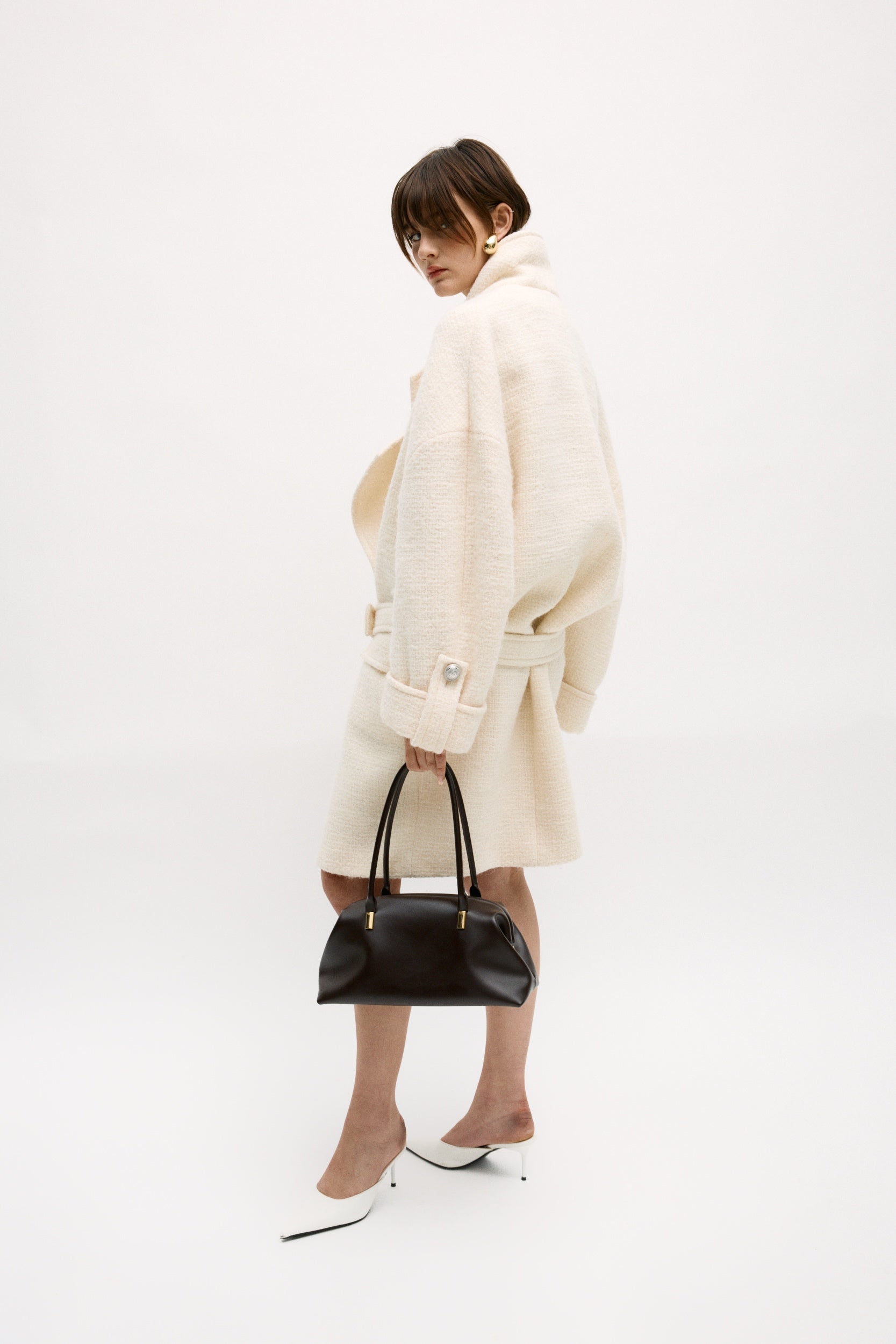 Person wearing a white coat and holding a Chocolate Medium Club Shoulder Handbag on a white background