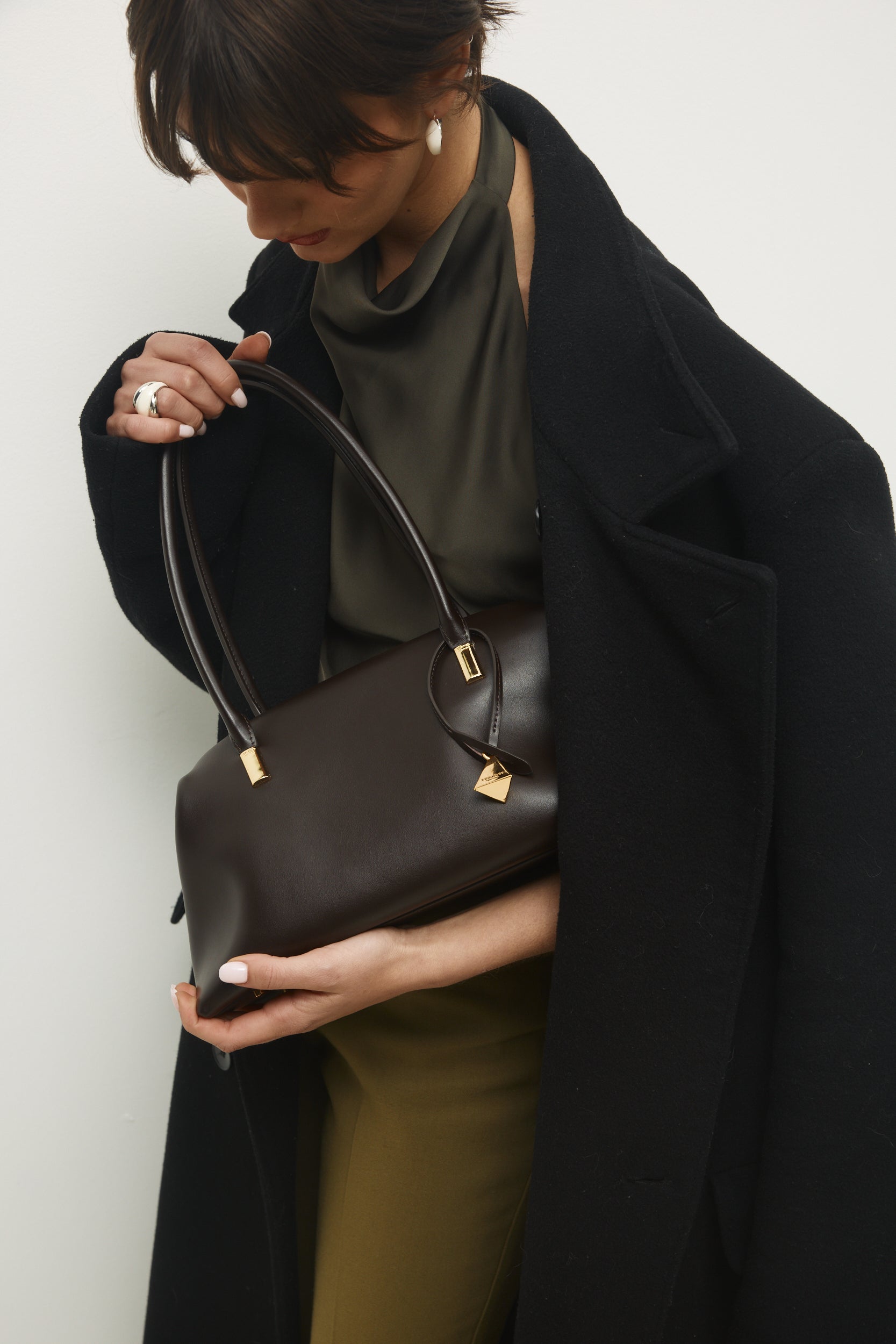 Person holding a Chocolate Medium Club Shoulder Handbag against a plain background