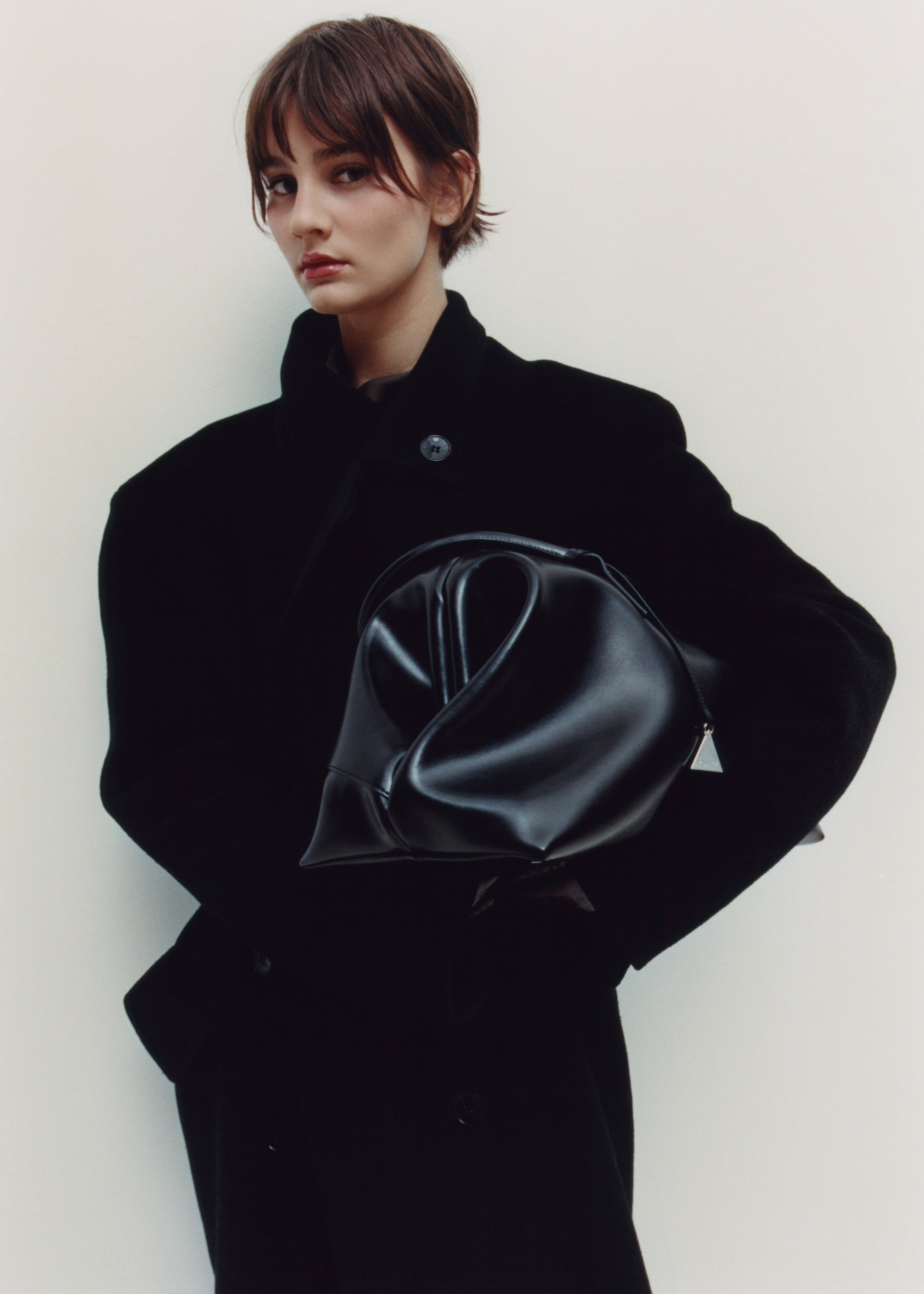 Person wearing a black coat holding a Black Club Large Handbag against a white background