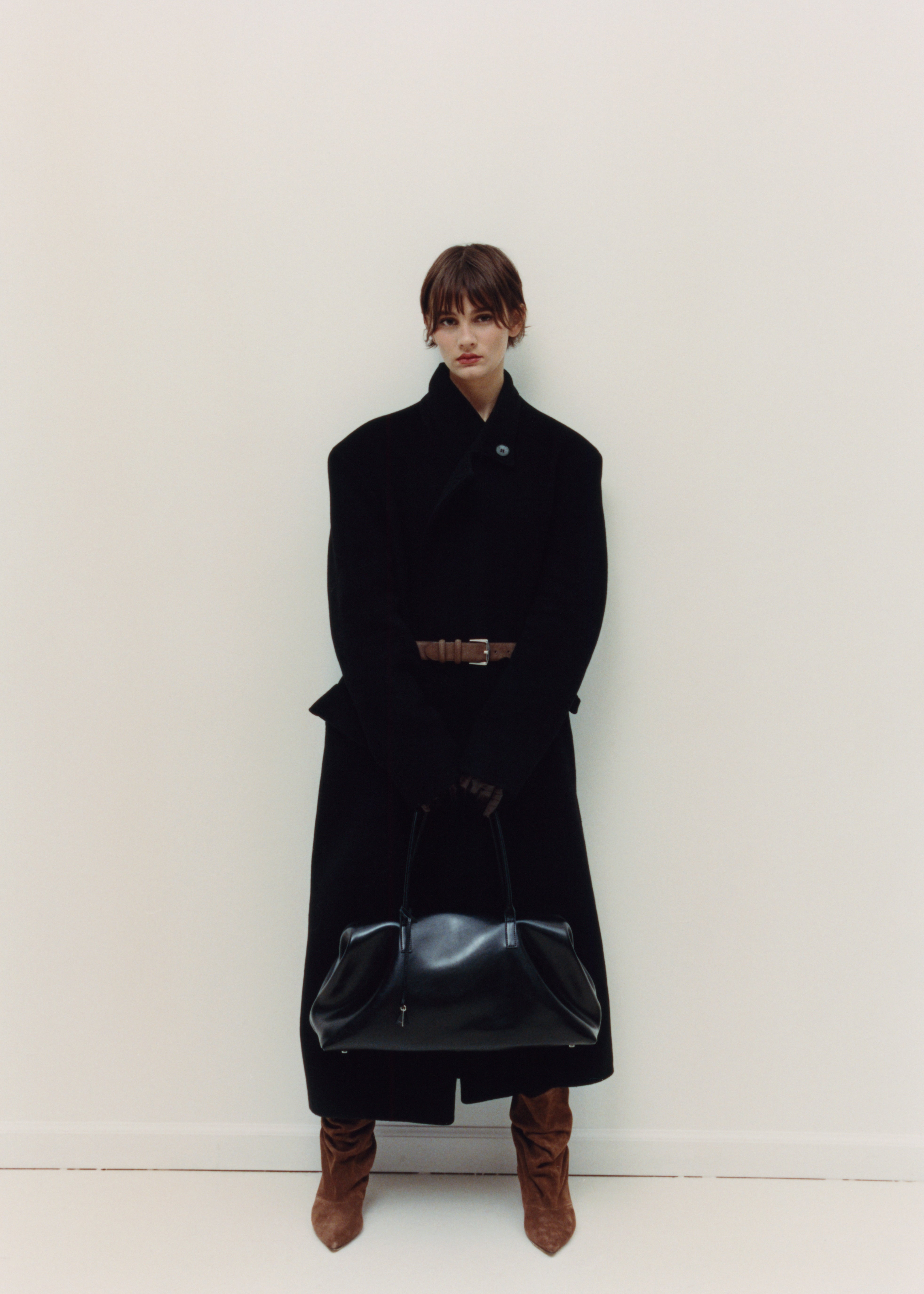 Person wearing a long black coat with a white background with a Black Club Large Handbag