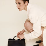Woman in a white outfit holding a Silver Noir Éclair Clutch Shoulder Handbag (Black) on a plain background