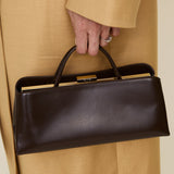 Person holding a Chocolate Éclair Clutch Shoulder Handbag with gold accents, wearing a beige coat.