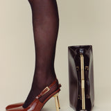 Brown high-heeled shoes with gold zipper detail next to a black shoe box on a beige background