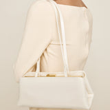Person wearing a beige dress with a matching Gold Ivory Éclair Bag: White Clutch Handbag on a plain background