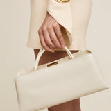 Hand holding a Gold Ivory Éclair Bag: White Clutch Handbag with gold accents against a neutral background