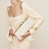 Woman in a light yellow dress holding a matching Gold Ivory Éclair Bag: White Clutch Handbag against a neutral background