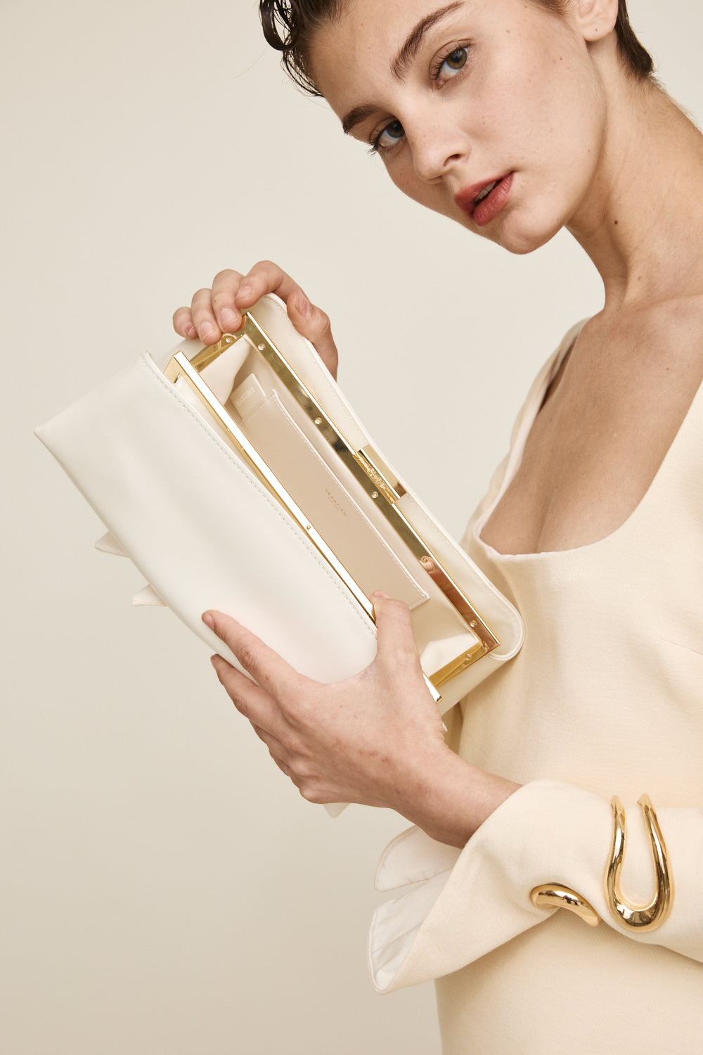 Woman holding a Gold Ivory Éclair Bag: White Clutch Handbag with gold accents against a plain background