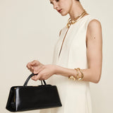 Woman holding a Gold Noir Éclair Clutch Shoulder Handbag (Black) against a plain background