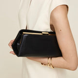 Person holding a Gold Noir Éclair Clutch Shoulder Handbag (Black) with gold accents against a neutral background