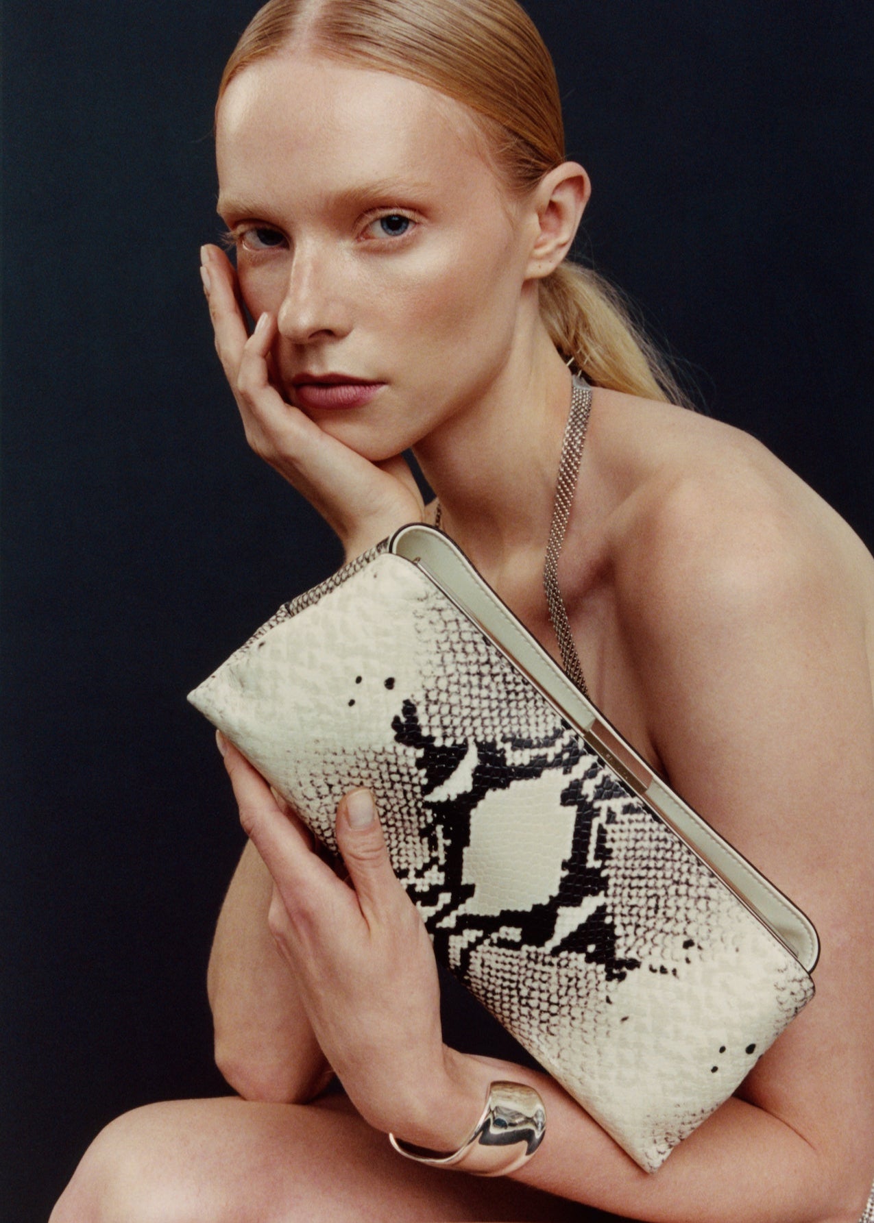 Woman holding a patterned clutch against a dark background