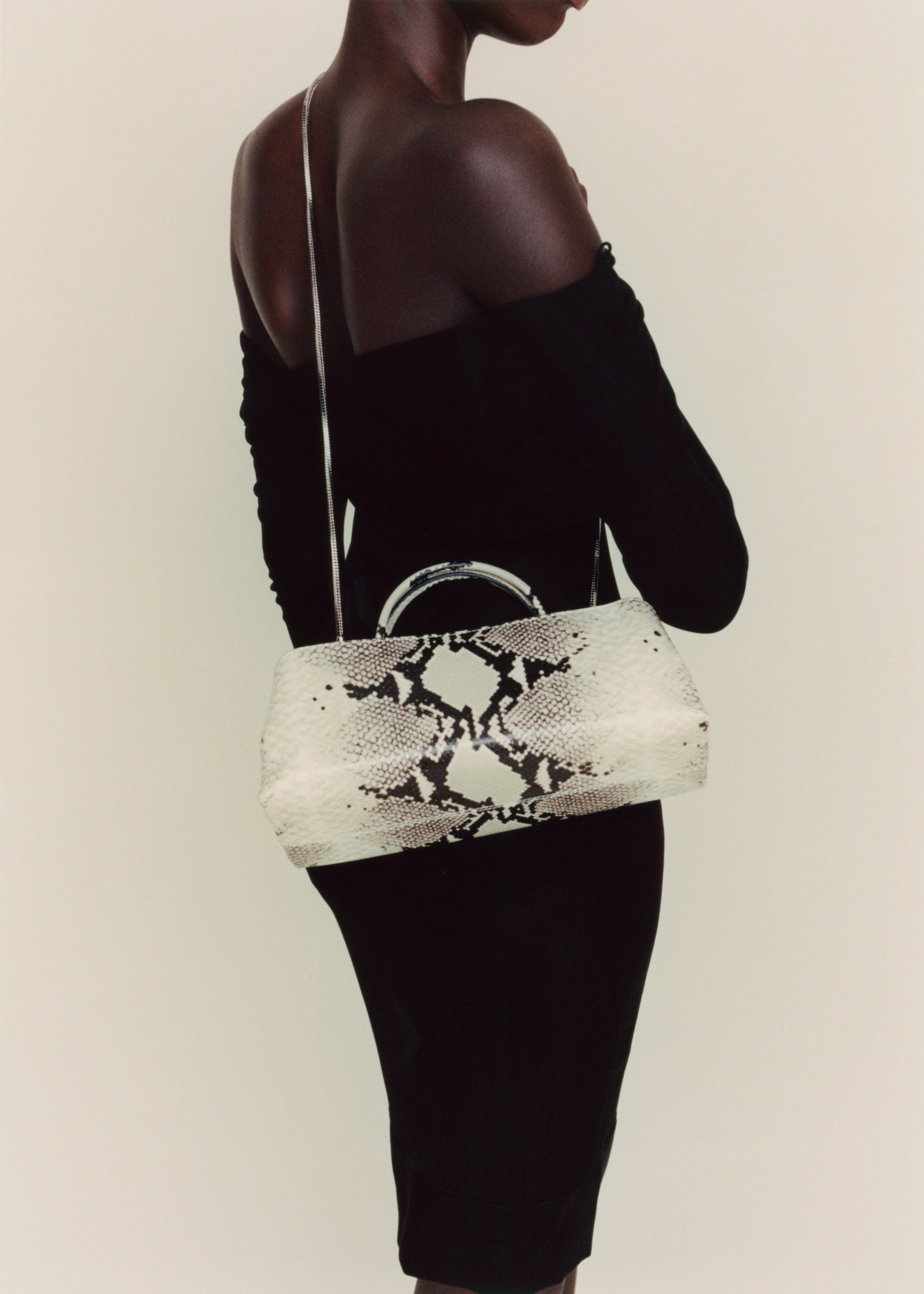 Person wearing a black off-shoulder top and holding a Python Éclair Clutch Shoulder Handbag with black snake print pattern.