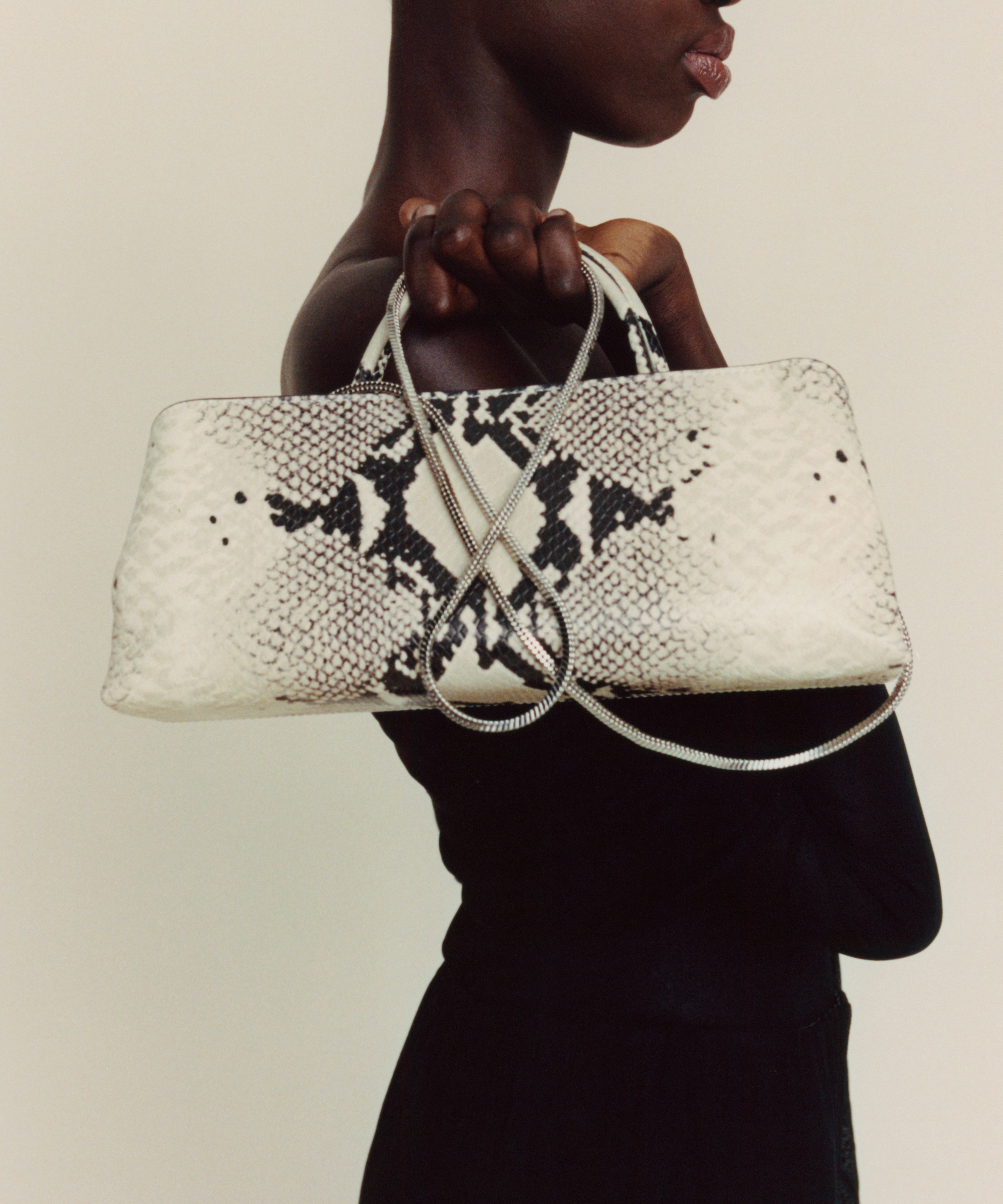 Woman holding a Python Éclair Clutch Shoulder Handbag with black snake print pattern against a beige background