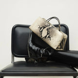 Python Éclair Clutch Shoulder Handbag on a black chair against a white background.