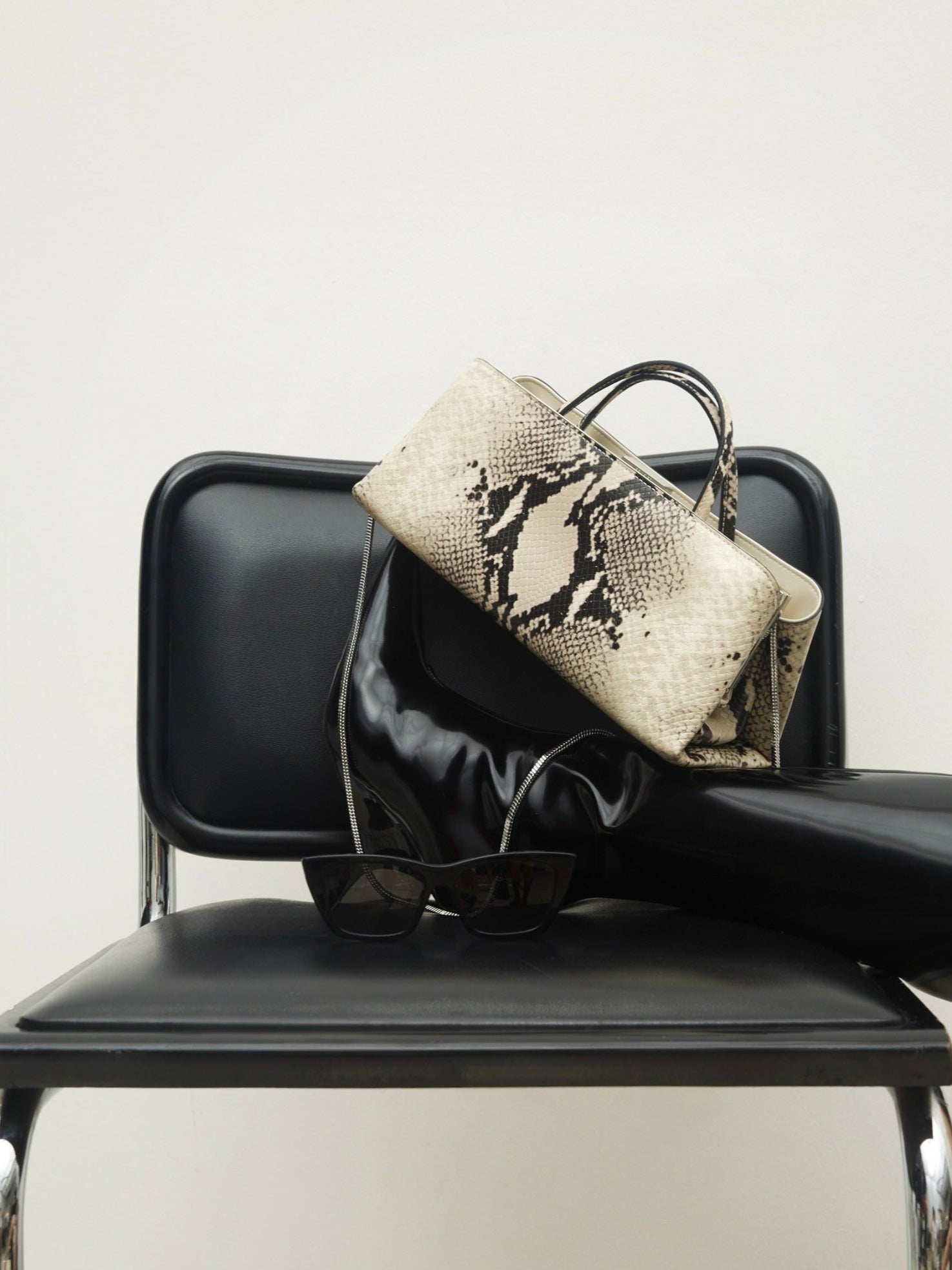 Python Éclair Clutch Shoulder Handbag on a black chair against a white background.