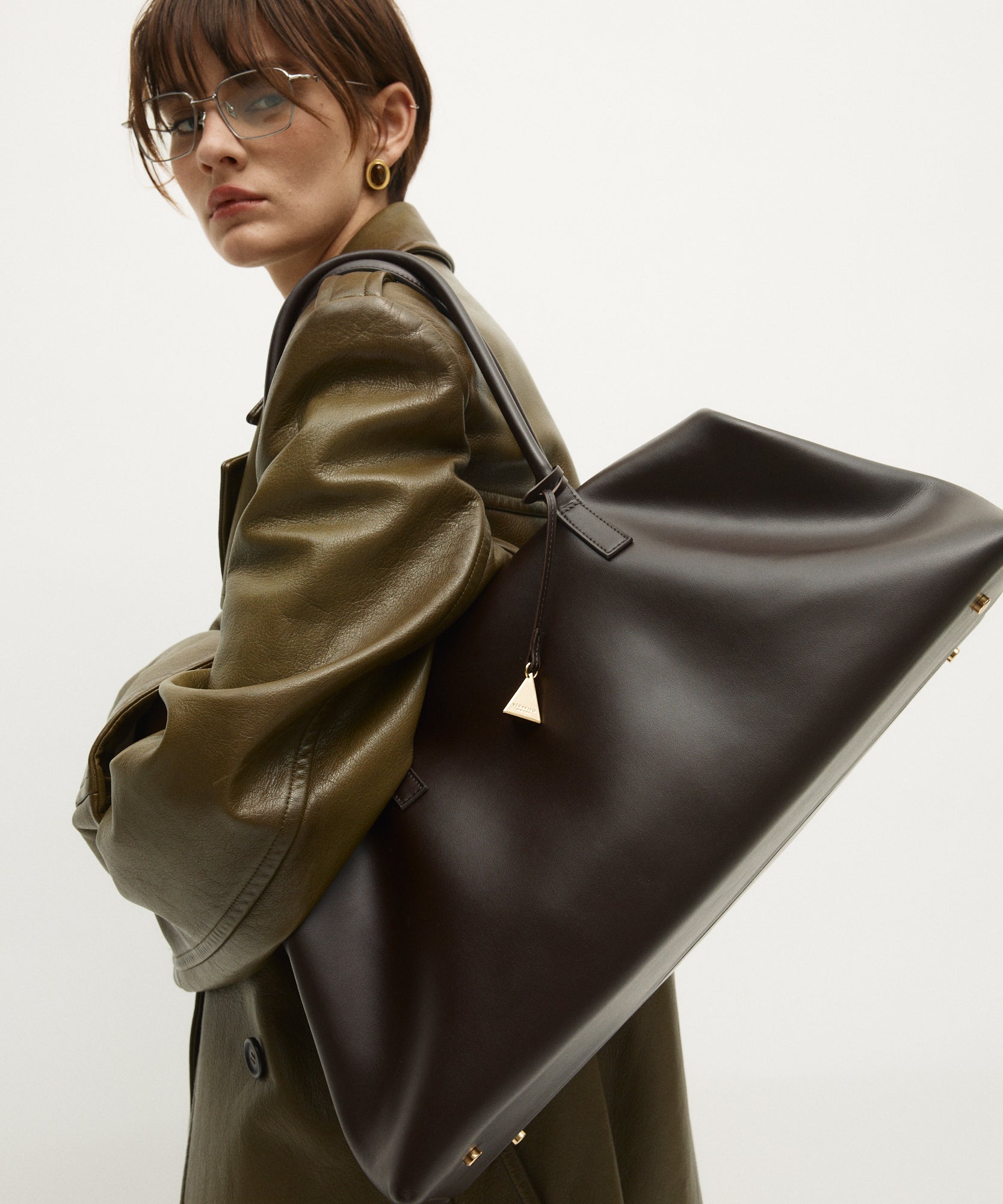 Person wearing a green coat holding a large Chocolate Club Large Handbag against a white background