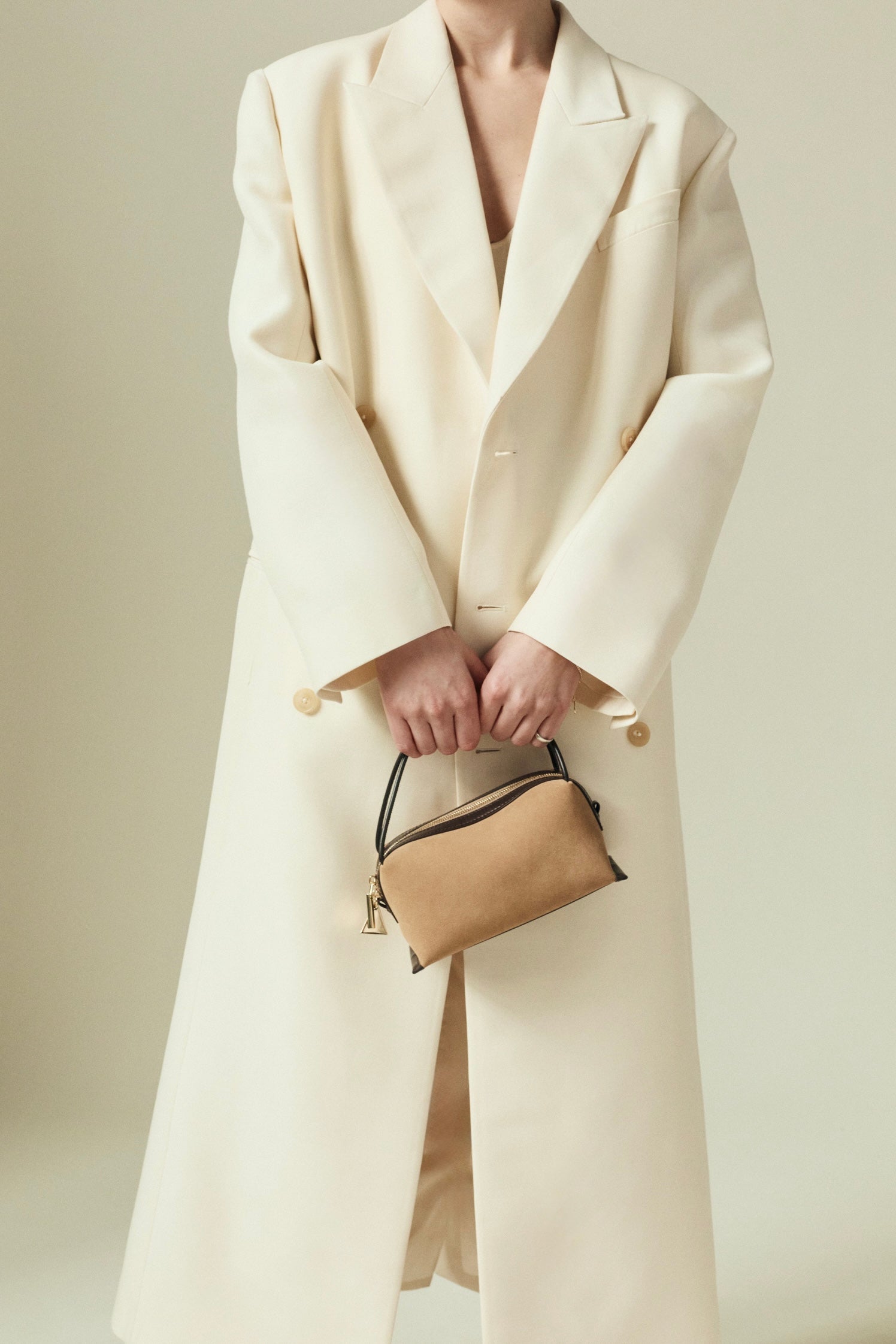 Person wearing a long cream coat holding a Verafied New York Gold Suede Café Mini Handbag against a neutral background