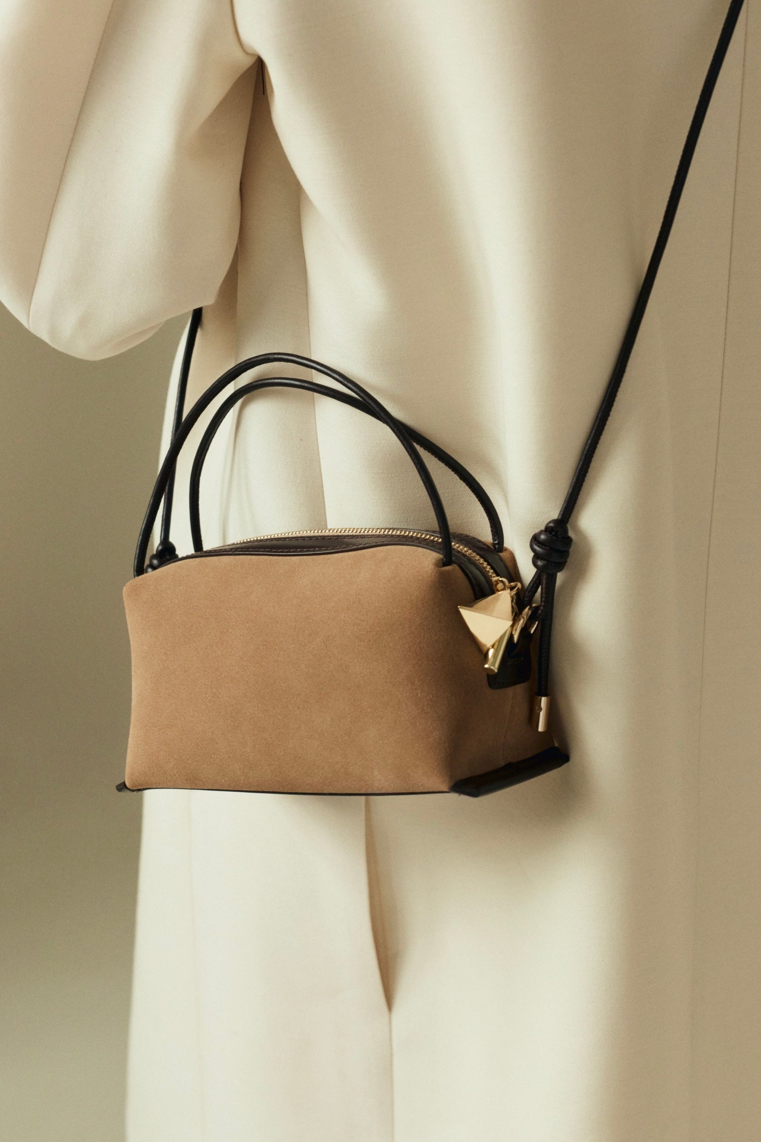 Verafied New York Gold Suede Café Mini Handbag with black strap held by a person wearing a beige coat.