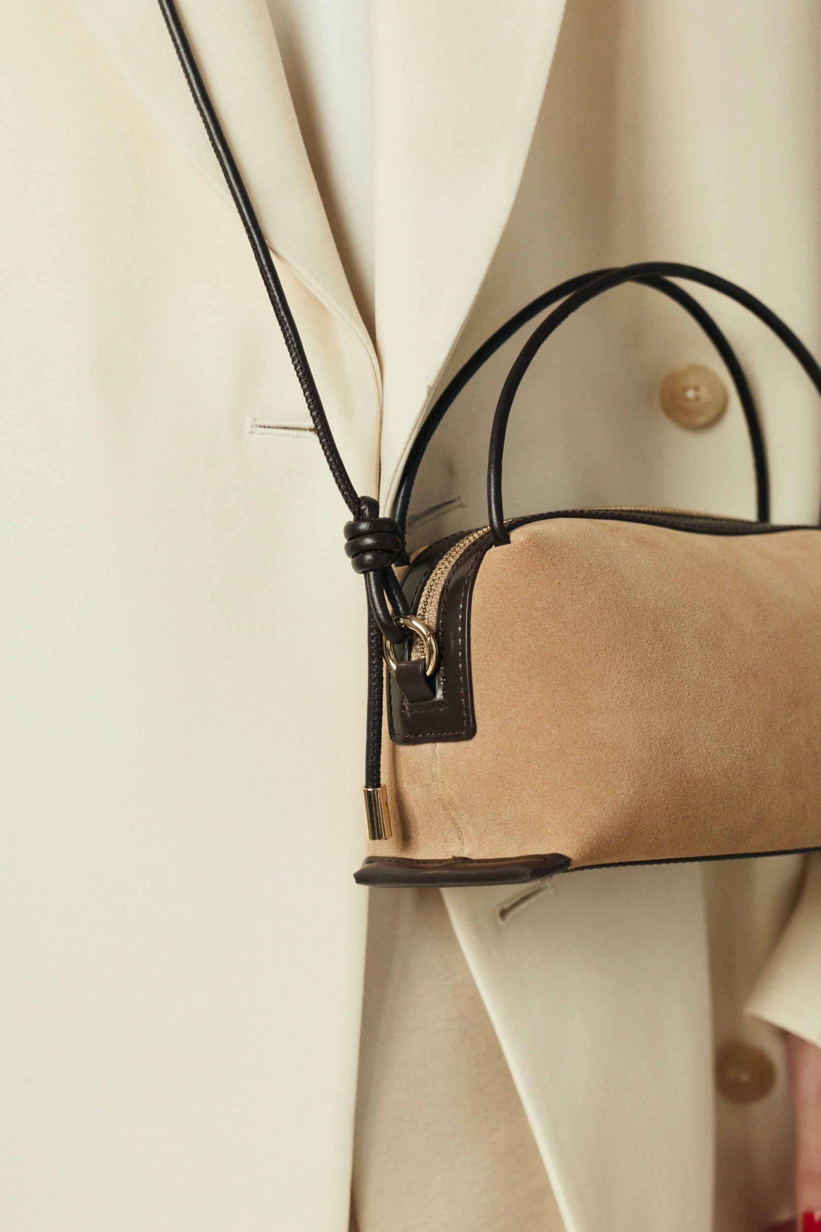 Close-up of a Verafied New York Gold Suede Café Mini Handbag with black accents on a light-colored coat.