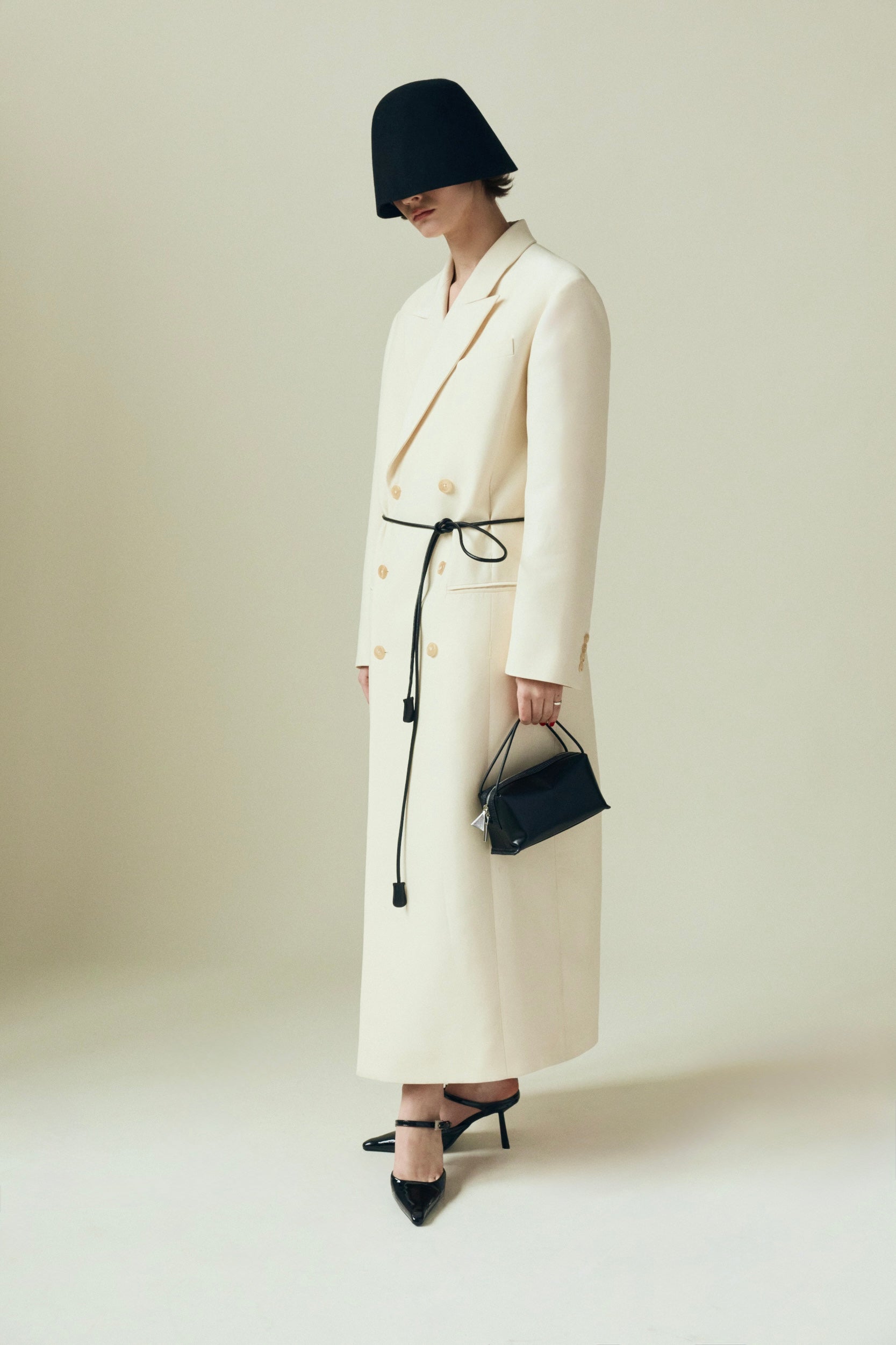 Person wearing a long white coat and black hat holding a Verafied New York Black Lizard Café Mini Handbag on a plain background