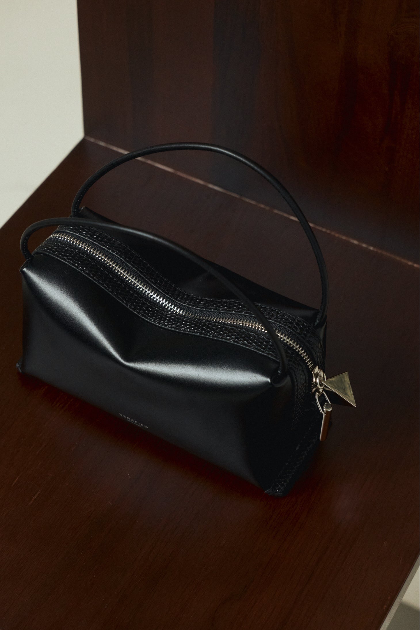 Verafied New York Black Lizard Café Mini Handbag with a gold zipper on a wooden surface