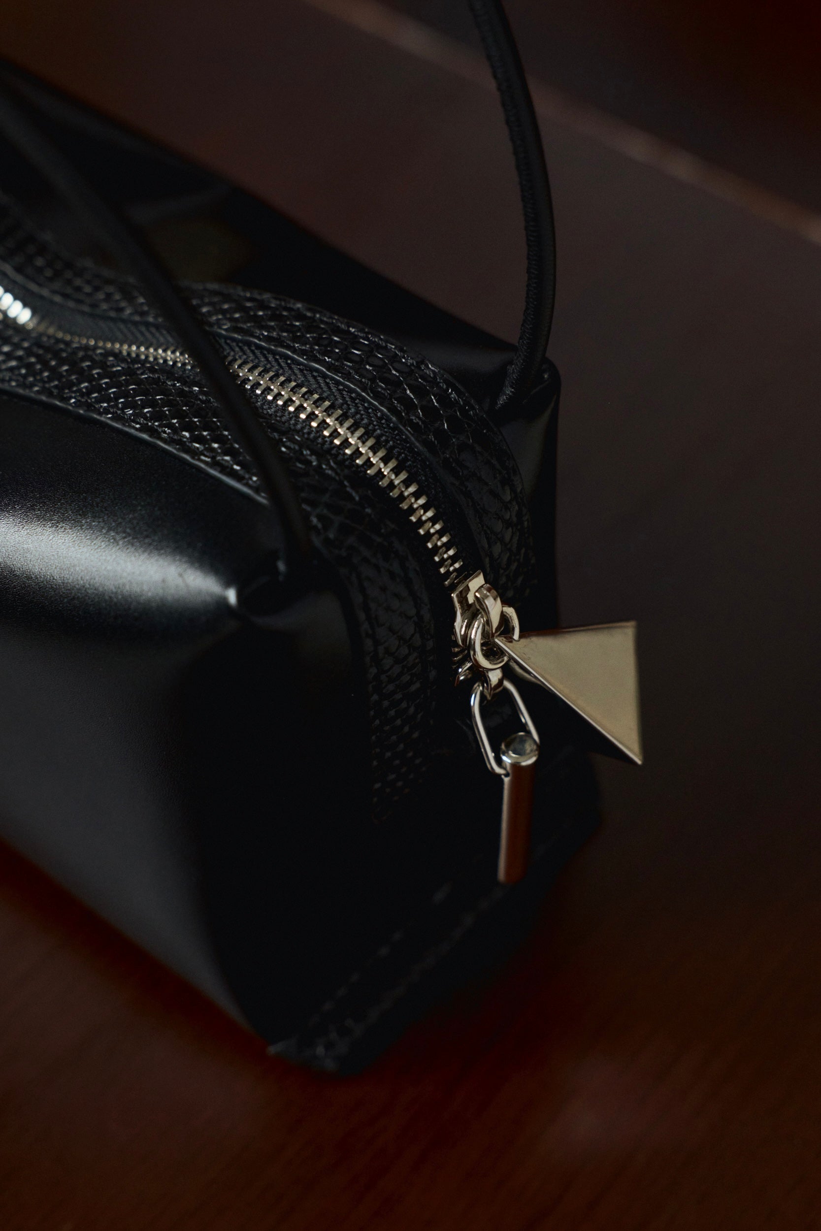 Close-up of a Verafied New York Black Lizard Café Mini Handbag with a silver zipper pull on a dark background