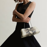 Woman holding a patterned Python Éclair Clutch Shoulder Handbag  against a plain background