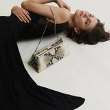 Woman in a black dress lying on a white floor with a Python Éclair Clutch Shoulder Handbag 