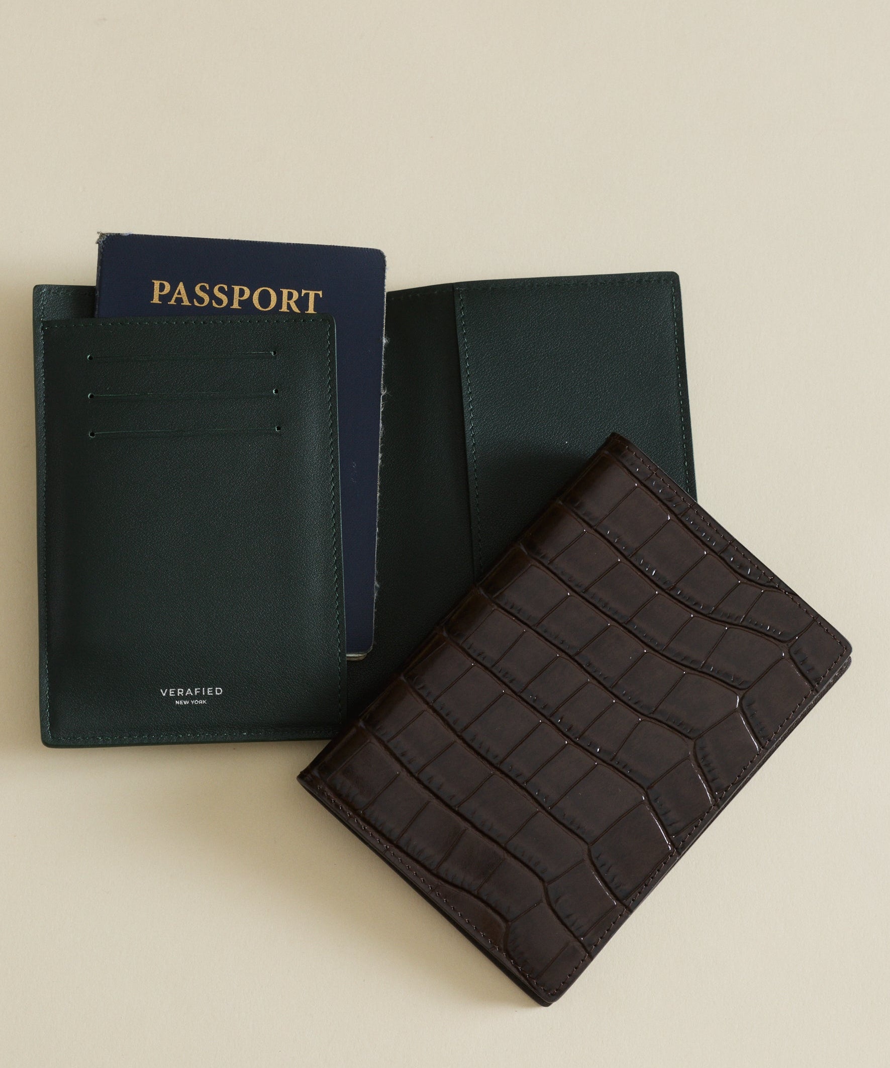 Black passport holder with a passport and Mocha Croc Embossed Passport Cover Wallet on a beige background