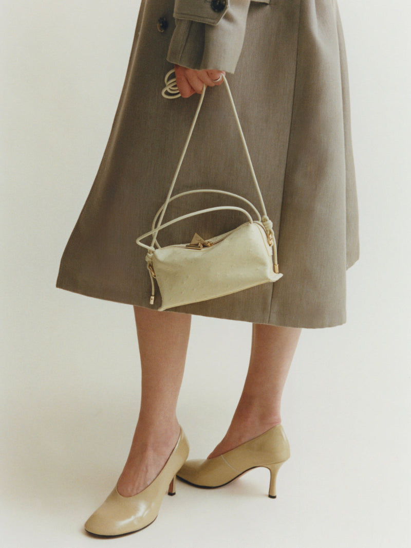 Person holding a beige Butter Ostrich Café Mini Bag: Crossbody Handbag wearing a long coat and matching shoes on a plain background