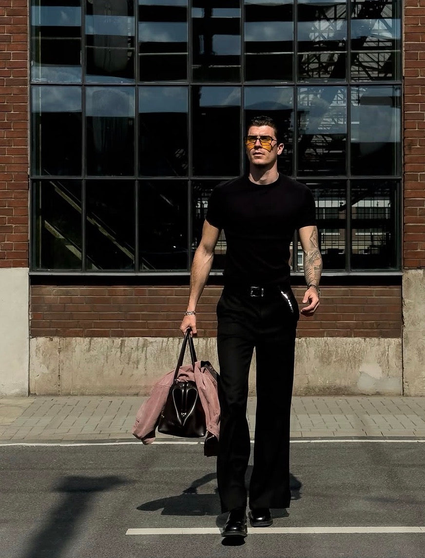 Man in black outfit walking on a street with a building in the background, holding a Black Club Bag: Work Bag for 15'' Laptop.