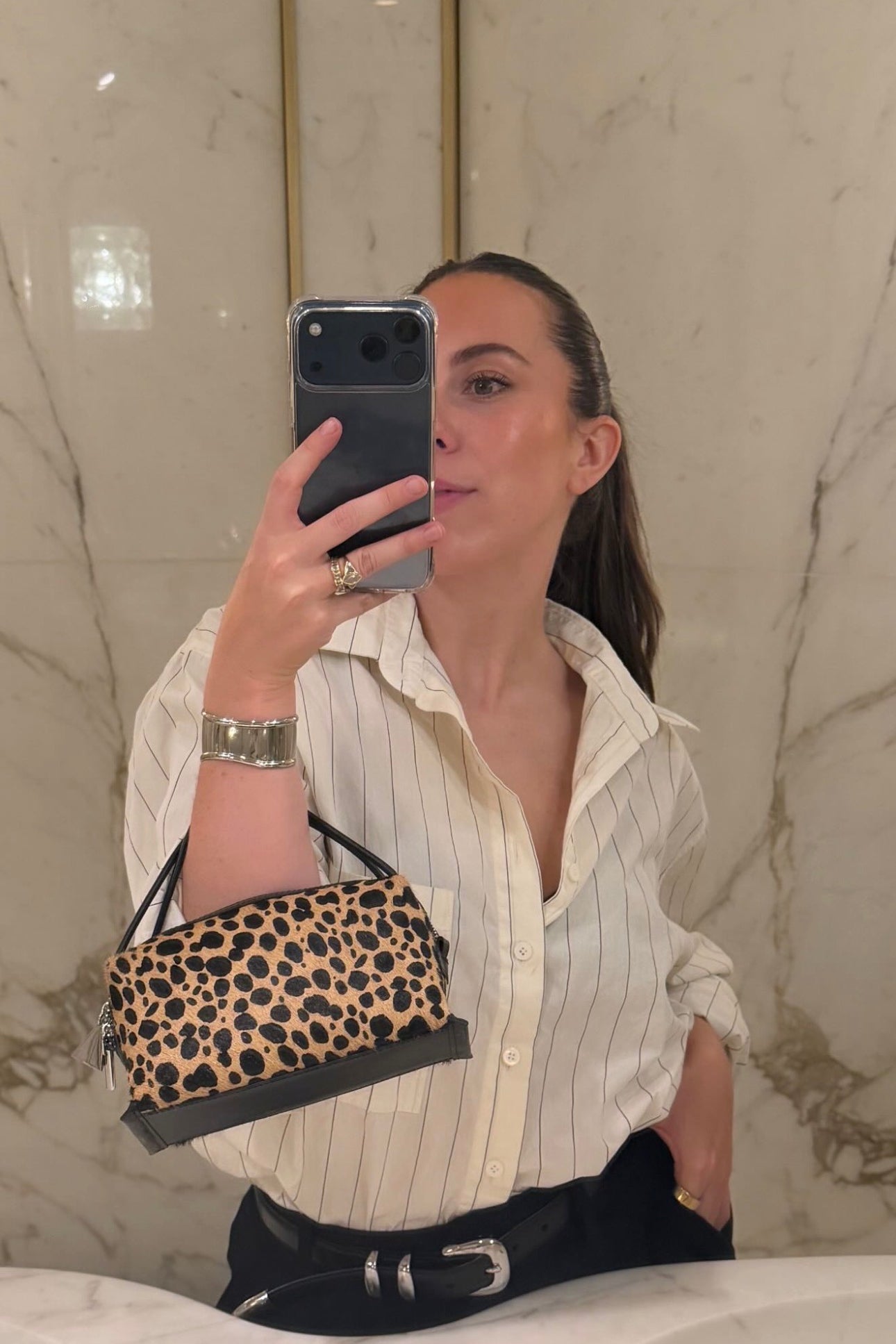 Person holding a leopard print Cheetah Calf Hair Café Mini Crossbody Handbag in front of a marble wall