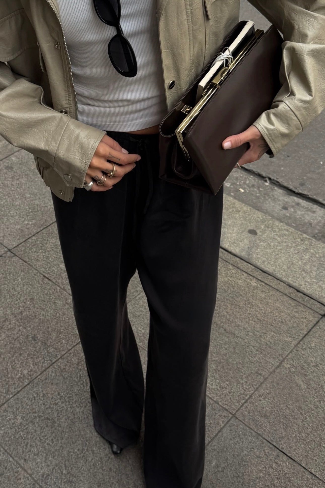 Person wearing a beige jacket, white shirt, black pants, and holding a brown Espresso Suede Éclair Bag: Clutch Handbag on a sidewalk.