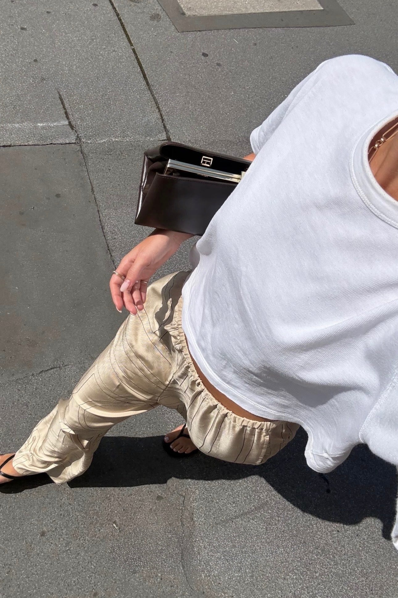 Person wearing a white hoodie and beige pants on a sidewalk, with a Espresso Suede Éclair Bag: Clutch Handbag.