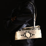 Python Éclair Clutch Shoulder Handbag with snake skin pattern held by a person wearing a black leather outfit.