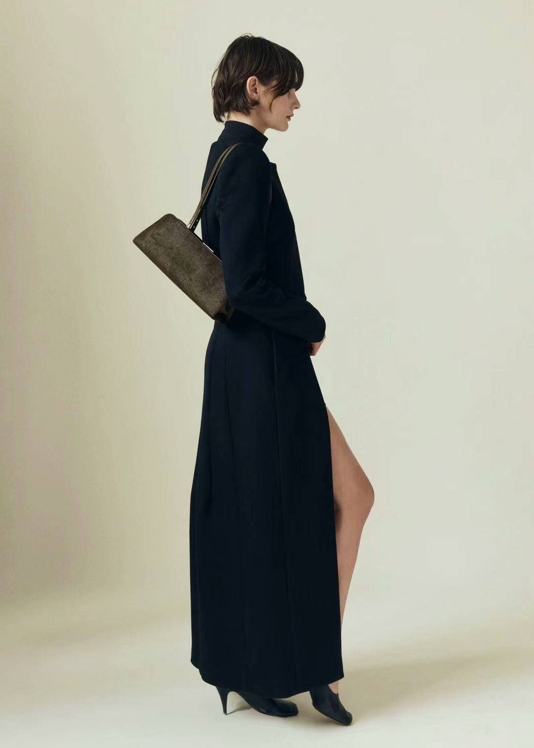 Woman wearing a long black dress with a slit, holding a Olive Calf Hair Clutch Shoulder Handbag against a plain background