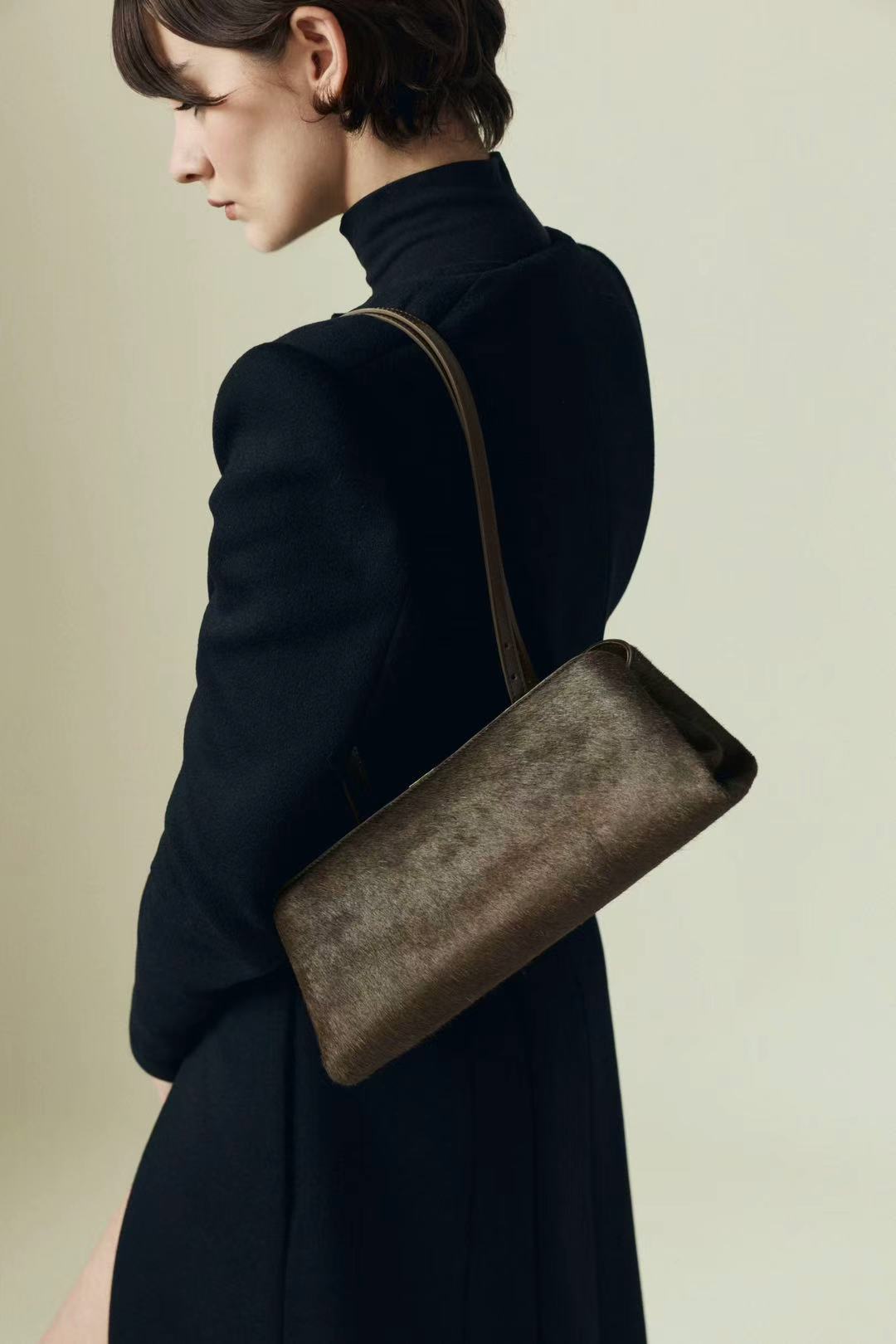 Person wearing a dark coat with a Olive Calf Hair Clutch Shoulder Handbag on a beige background